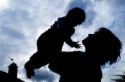 Silhouette of woman holding infant above her head.